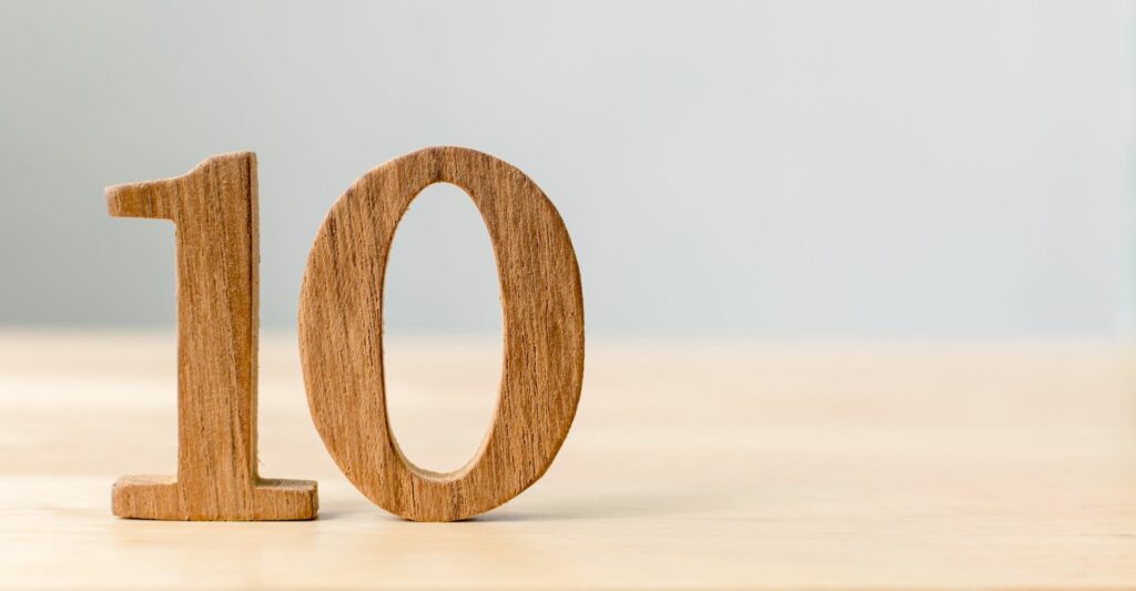 A wooden 3d carved number '10' is standing on top of a blurred out light wooden table on the left hand side of the frame.