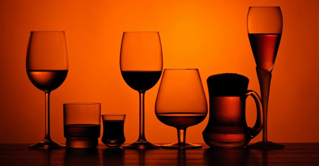 A photograph of seven different wine/alcohol glasses laid out in a row with an overlay of an orange tinge.