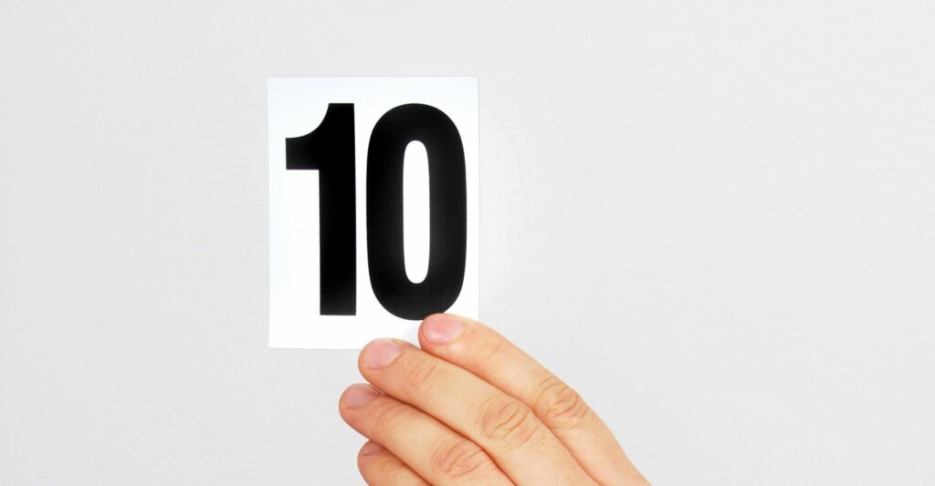 A photo of a person's fingers holding onto a white card with a black, bold number '10' on it,