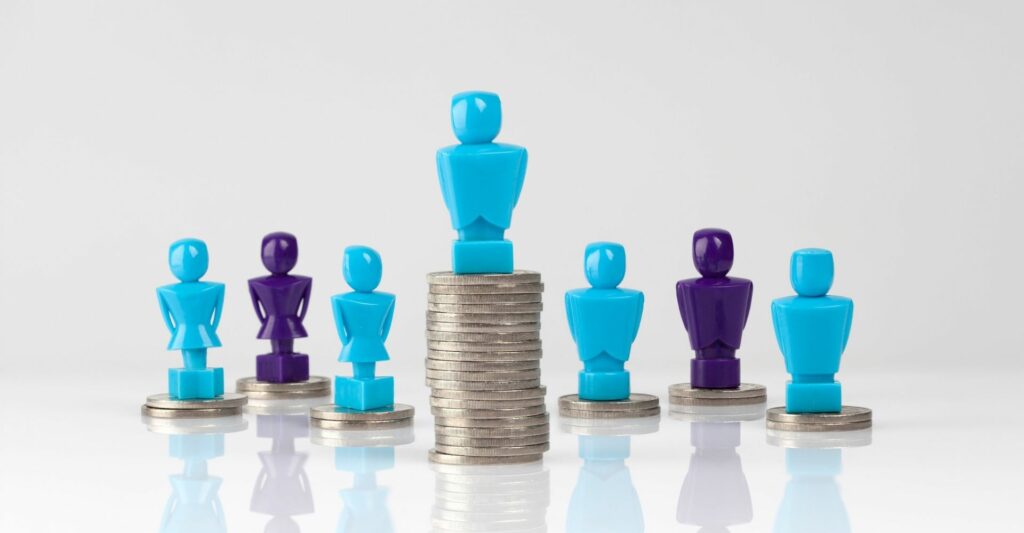 A small blue pawn statue standing on top of a large stack of coins in the middle of the image, and behind it are six other blue and purple pawns standing on top of a lower stack of coins.