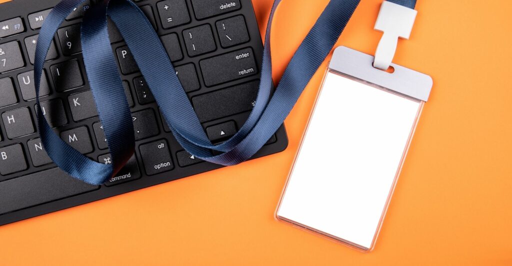 An image of a black computer keyboard and a blank white employee lanyard with a thick navy strap.