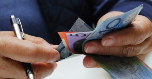 A close of photo of someone counting Australian money while holding a pen in their right hand.