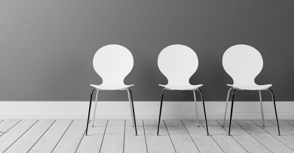 A photo of three empty white chairs with silver legs in a row