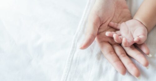 A close up image of a mother's hand underneath a baby's hands.
