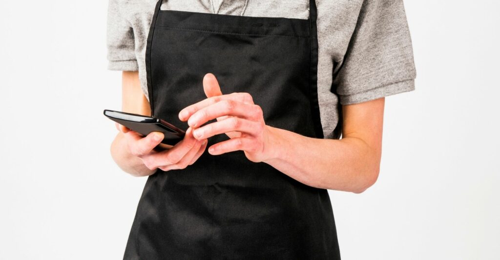 A photo of worker's torso who is wearing a black apron and holding a dark brown notebook - similar to the ones waitresses use to write down menu orders.