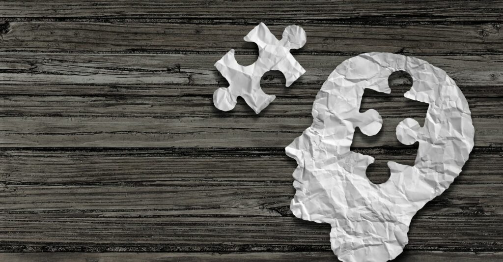 An image of a paper human head with a puzzle piece cut out of it, and the puzzle piece sits to the left hand side of the head.
