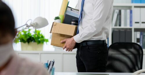 A half body shot of an employee holding a box of items after being terminated.