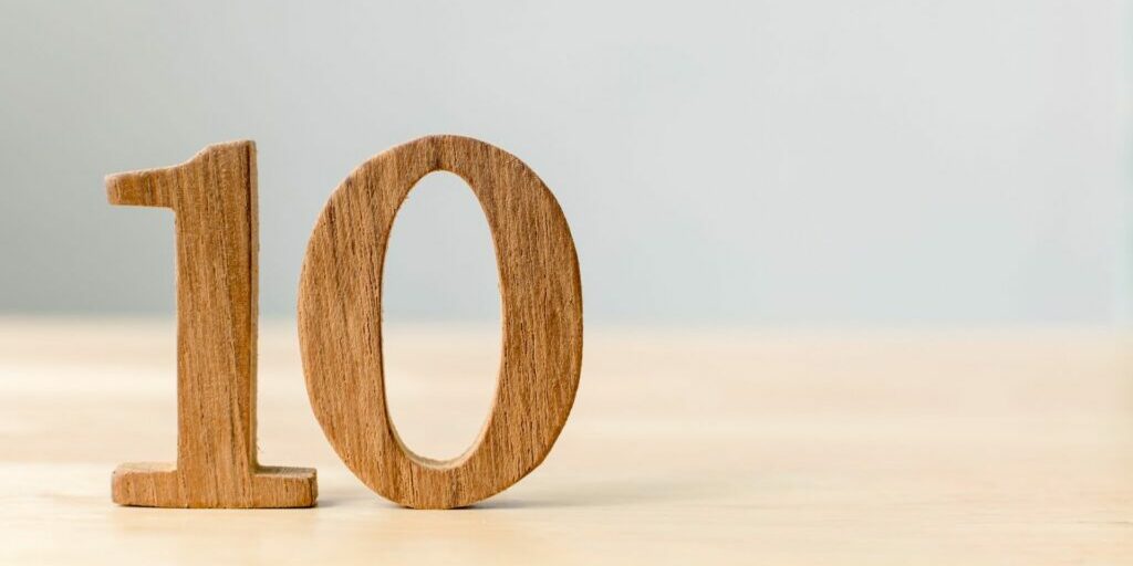 A wooden 3d carved number '10' is standing on top of a blurred out light wooden table on the left hand side of the frame.