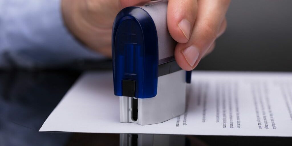 A close up image of someone stamping a document with a large metal stamp.