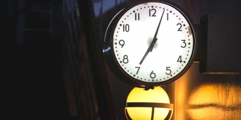 a black analogue clock with a white face, black numbers and black hands showing the time of 7:03.