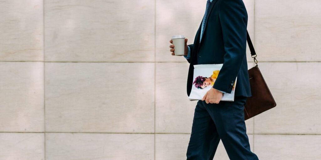 a photo of someone walking to work with a coffee in one hand and a magazine in the other.