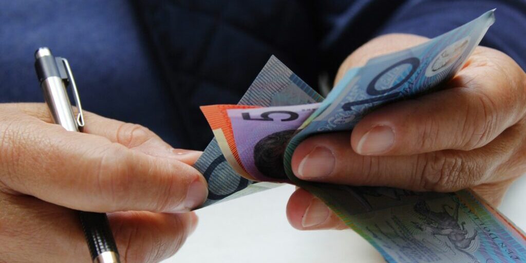 A close of photo of someone counting Australian money while holding a pen in their right hand.