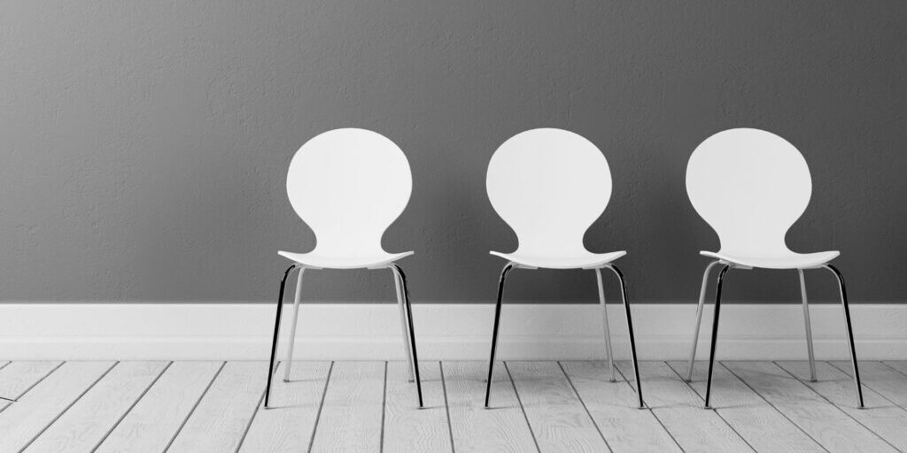 A photo of three empty white chairs with silver legs in a row