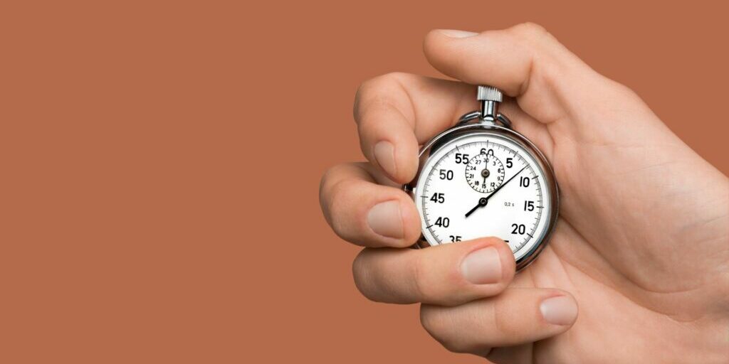 A close up image of a right hand holding a silver stopwatch with their thumb on the top counter.