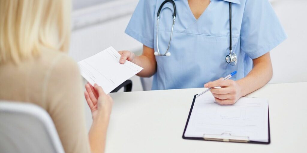 A photo of a doctor handing a lady a medical certificate over the table.