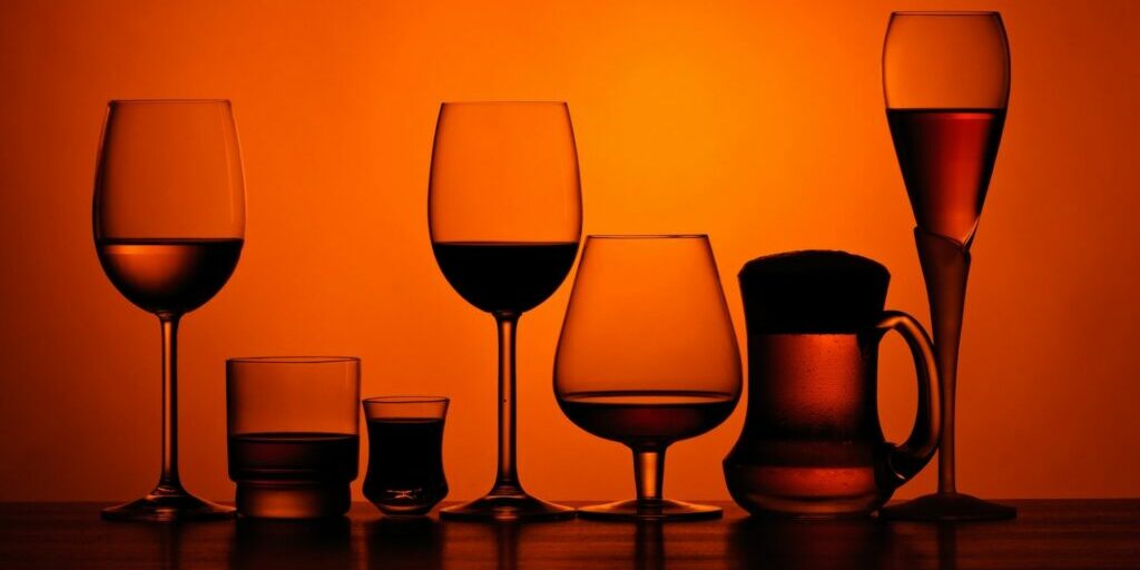 A photograph of seven different wine/alcohol glasses laid out in a row with an overlay of an orange tinge.
