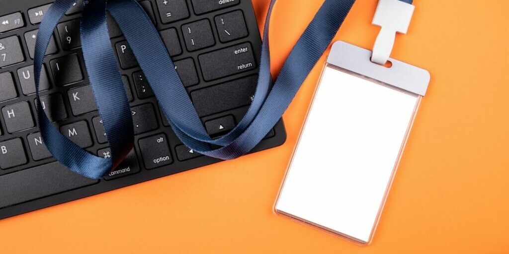 An image of a black computer keyboard and a blank white employee lanyard with a thick navy strap.