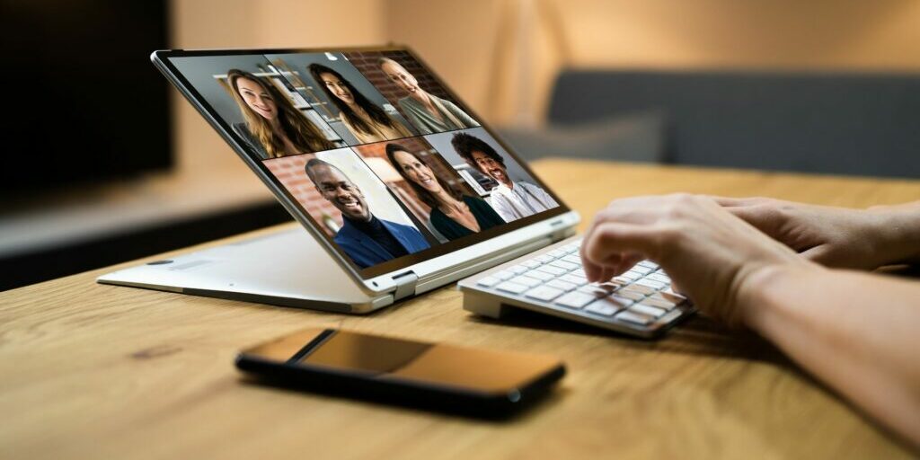 A photo of someone typing on a keyboard with their computer screen full of 6 people's faces as they video call.