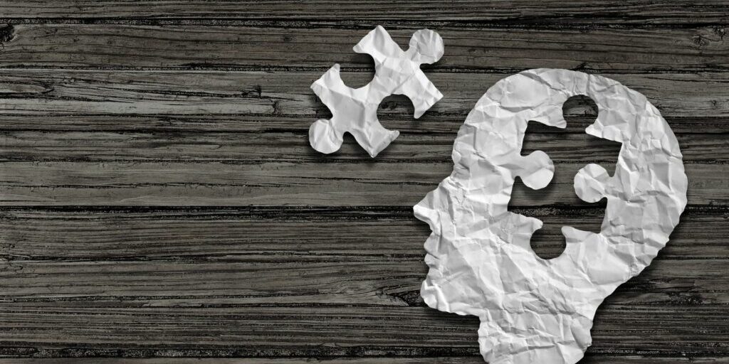 An image of a paper human head with a puzzle piece cut out of it, and the puzzle piece sits to the left hand side of the head.