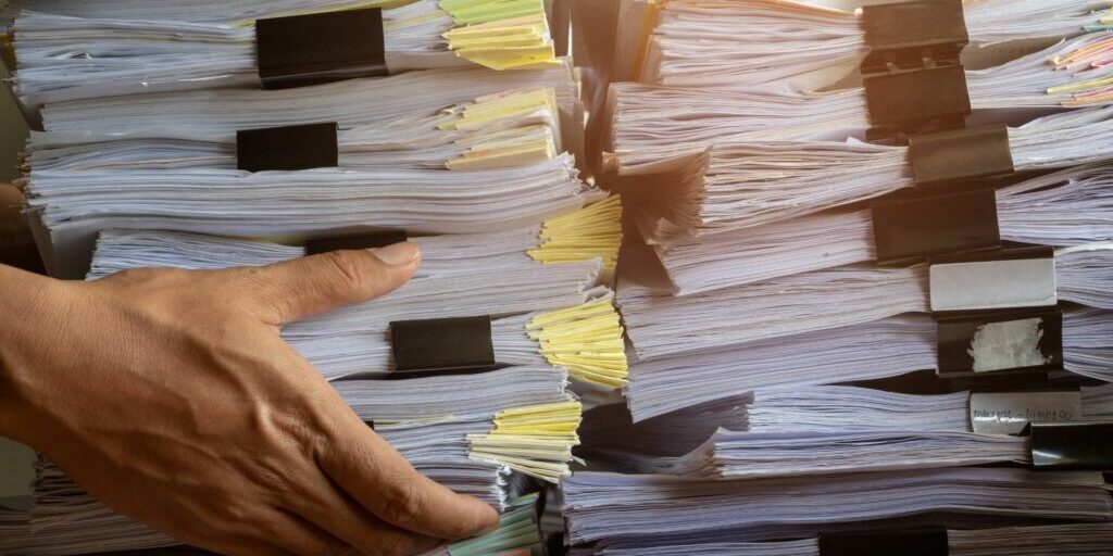 a photo showing someone's right hand going in to grab a pile of documents from an even larger pile of documents.