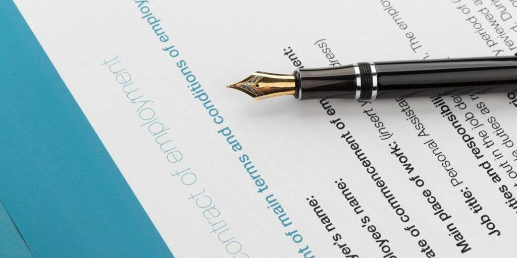a black fountain pen with a gold tip lying down on a piece of paper titled 'contract of employment'.
