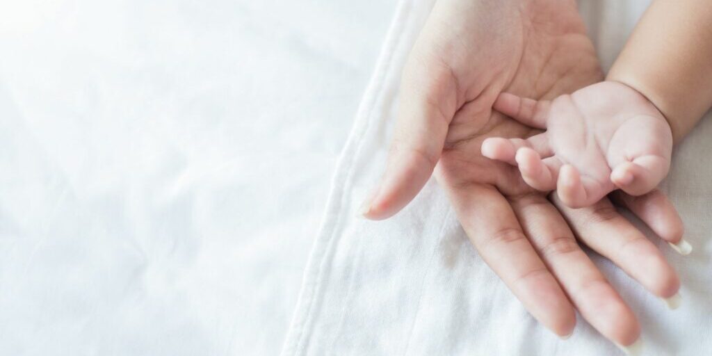 A close up image of a mother's hand underneath a baby's hands.