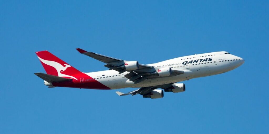A photo of a Qantas plane in mid-flight on a clear blue sky.