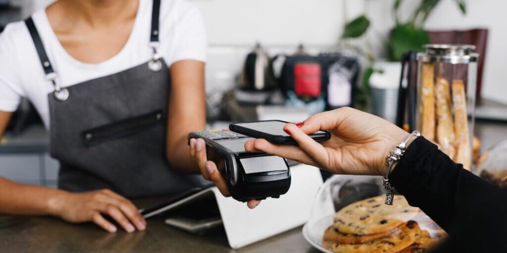 An image of a customer tapping their phone onto an eftpos machine to pay at a cafe.