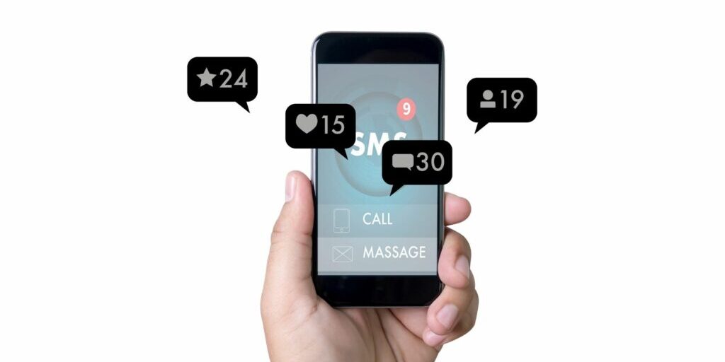 An image of a person holding up a black phone in their left hand with four speech bubble graphics coming out of the screen which are social media notifications for likes, starred, contacts and messages.