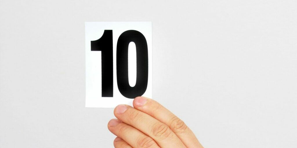 A photo of a person's fingers holding onto a white card with a black, bold number '10' on it,