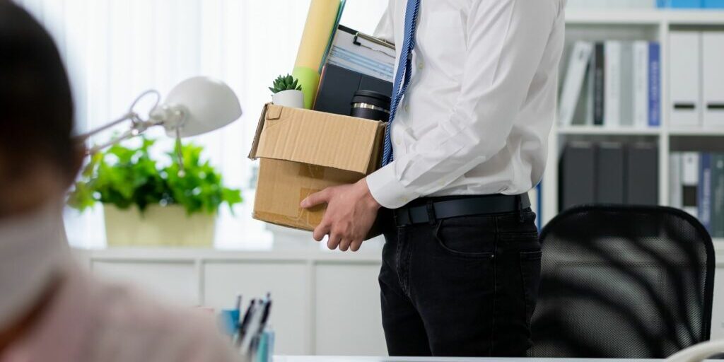 A half body shot of an employee holding a box of items after being terminated.