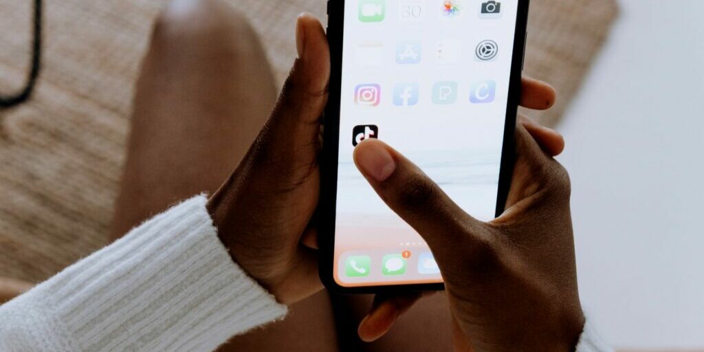 a close up shot of someone's hand holding their phone with their right hand thumb hovering over the tik tok app on their phone.