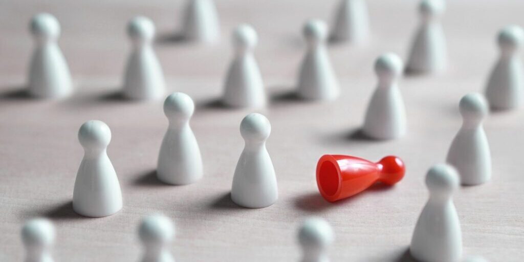 An image of little white game markers laid out randomly on a surface, with one red game marker knocked over in the crowd of the white ones.