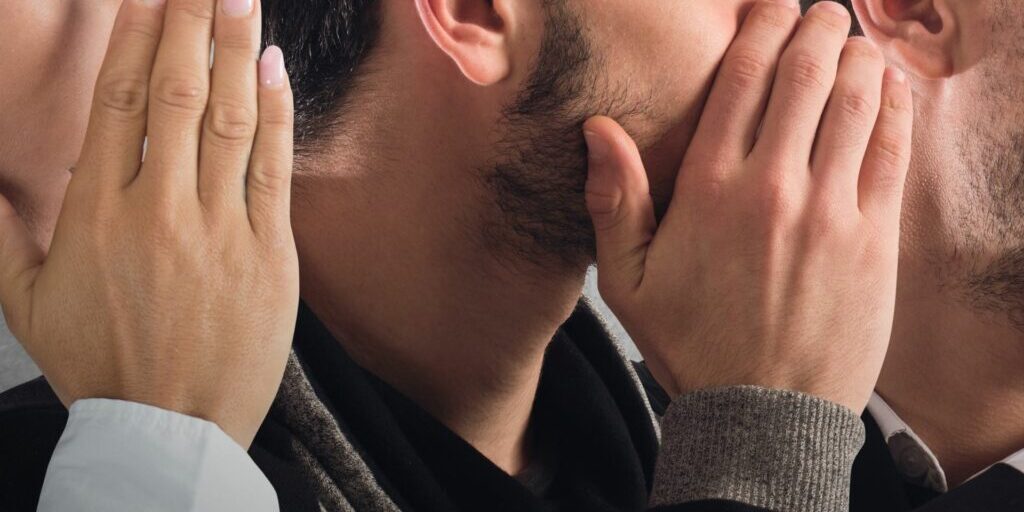 A close up image of 3 side profile faces. The left woman is covering her hand and whispering something to the man in the middle, and the man in the middle is whispering something to the man on the right,